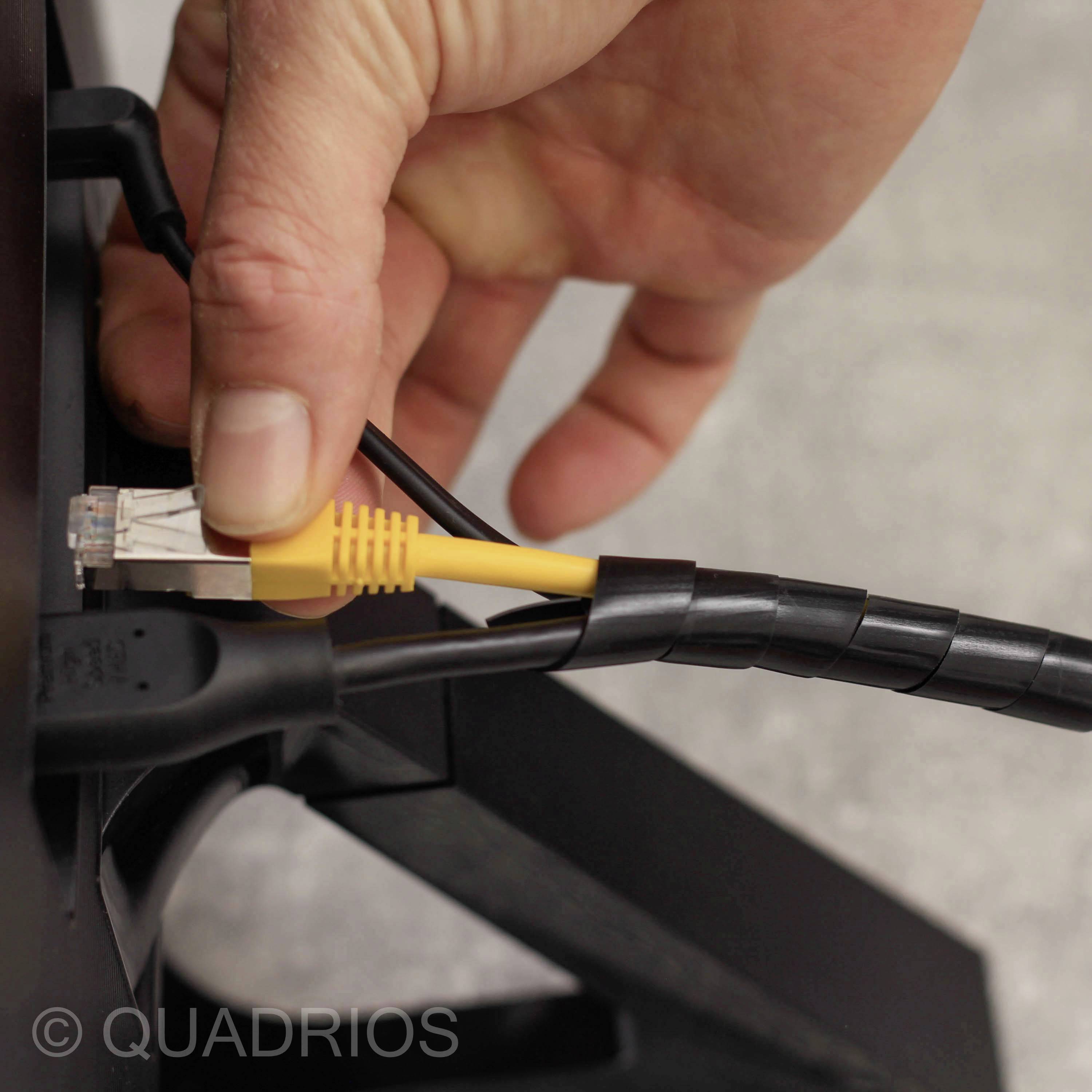 Eine Hand steckt ein gelbes Ethernet-Kabel in einen Router. Im Hintergrund verschwommene Geräte.
