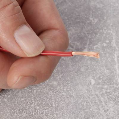 Eine Hand hält ein rotes Drahtkabel mit freigelegtem Kupferdrahtende über einer grauen Oberfläche. Hierbei handelt es sich um einen elektrischen Anschlussdraht.