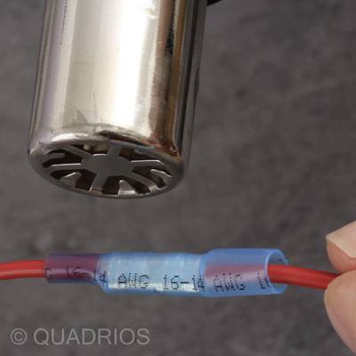 Eine Hand hält einen roten Draht mit einem blauen Verbinder, der mit einem metallischen Zylinder verbunden ist.