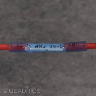 Ein blaues elektrisches Verbinderstück verbindet zwei rote Kabel. Auf dem Verbinder sind die Angaben '15-14 AWG' sichtbar.
