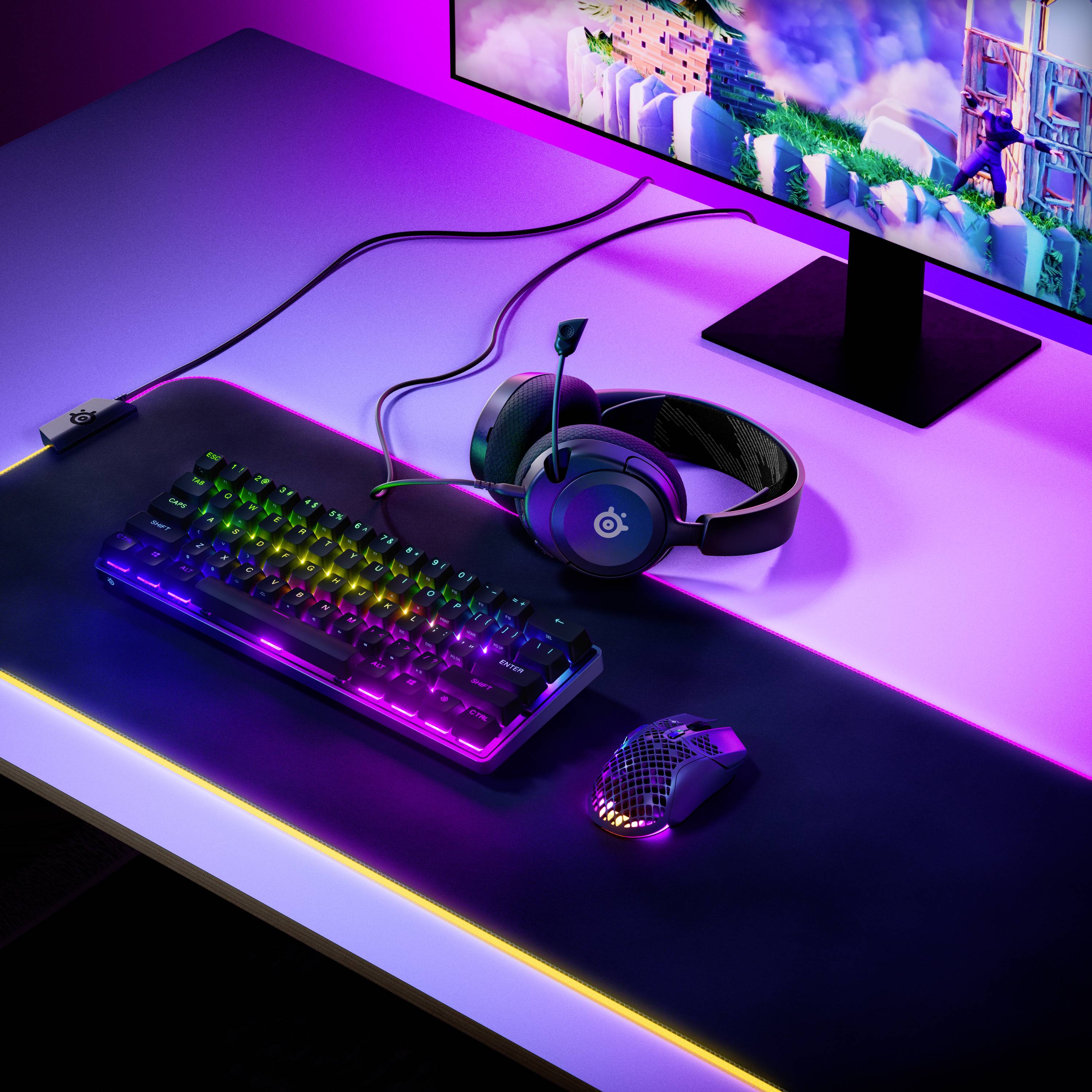 Computertisch mit Gaming-Tastatur, Maus, Headset und Monitor. Bunte RGB-Beleuchtung und virtuelle Landschaft auf dem Bildschirm.
