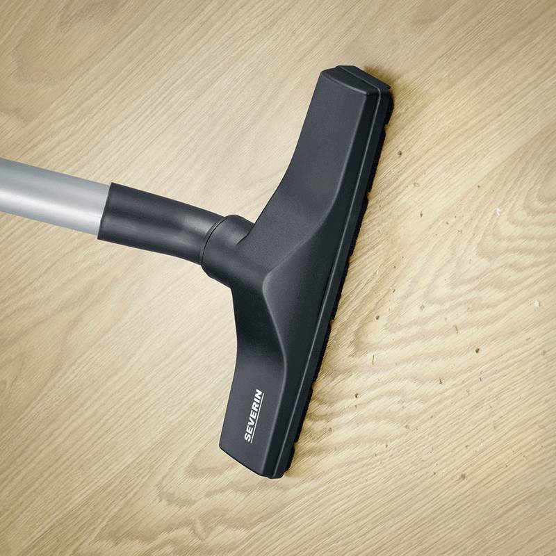 Ein Staubsauger saugt Krümel von einem Holzfußboden auf.