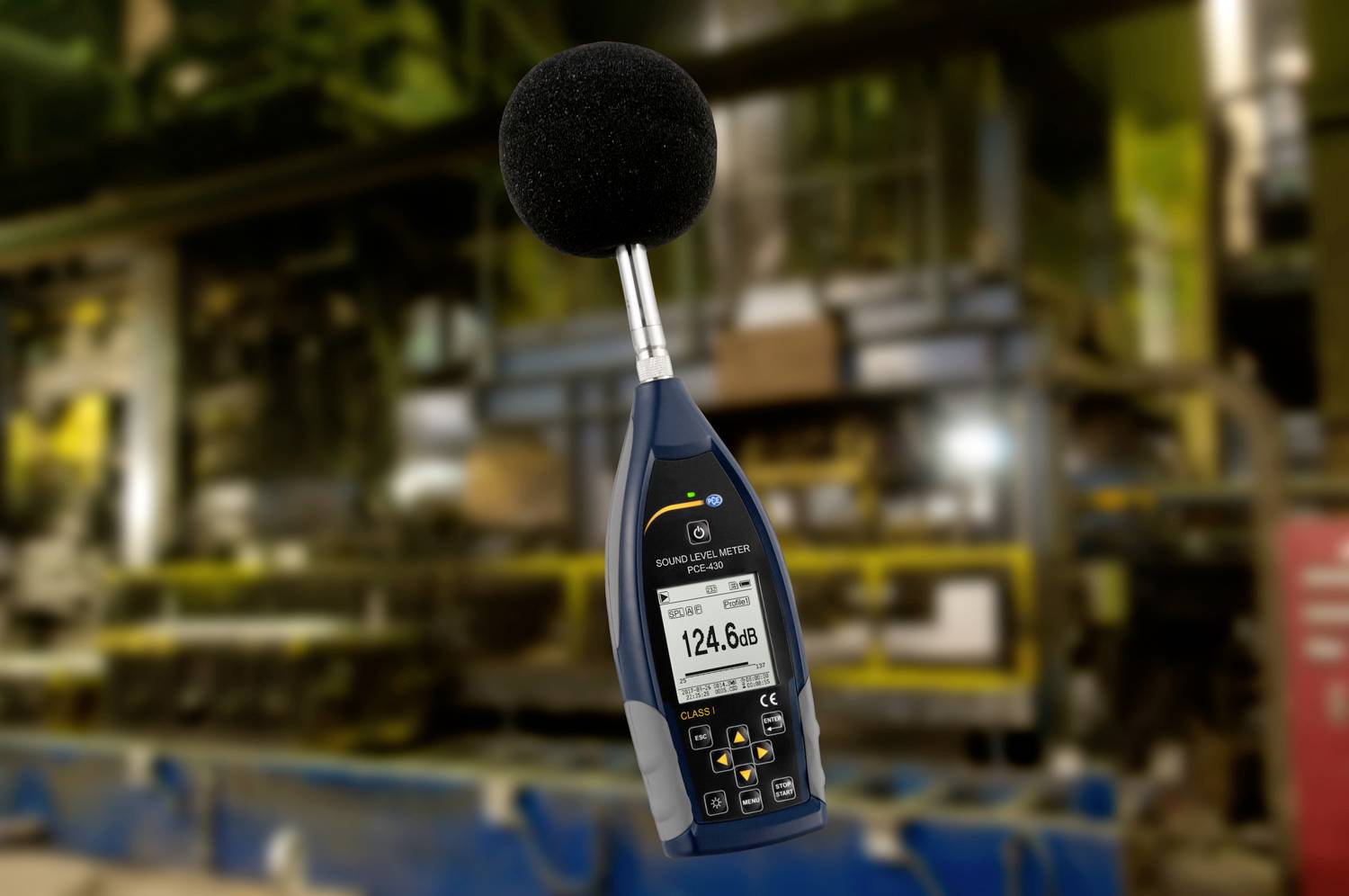 Ein Schallpegelmessgerät zeigt einen Wert von 124,6 dB in einer Fabrikumgebung an. Hintergrund unscharf, Fokus auf Messgerät.