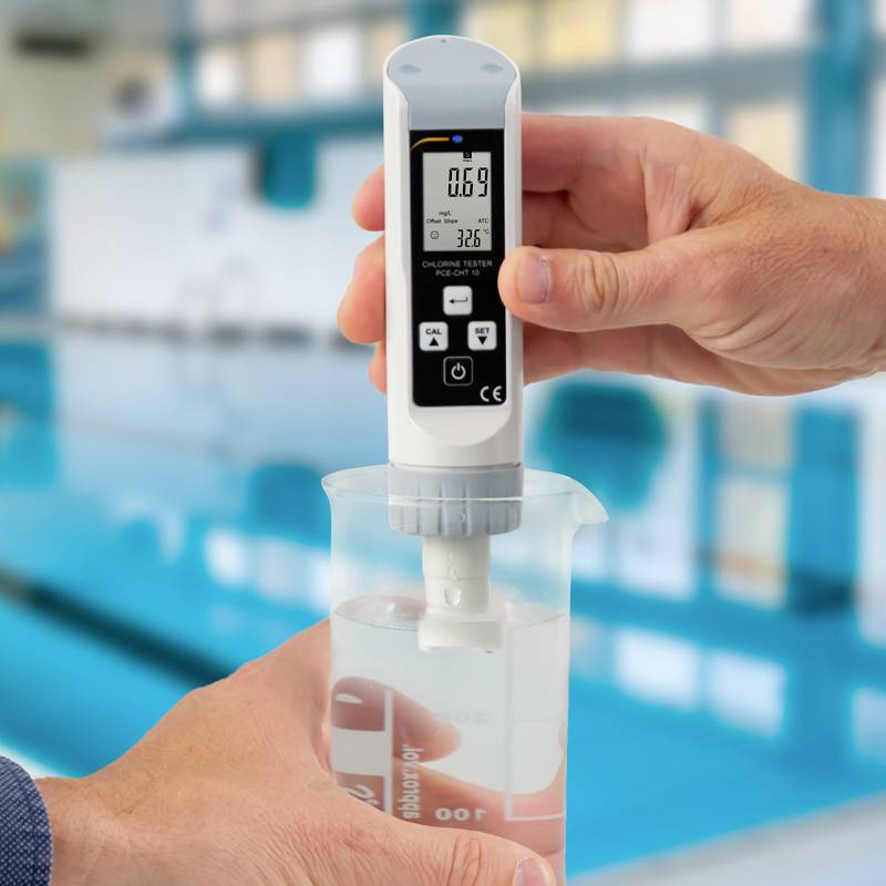 Eine Hand hält ein digitales Messgerät, das 0,69 pH und 32,5°C anzeigt. Im Hintergrund verschwommen ein Pool.