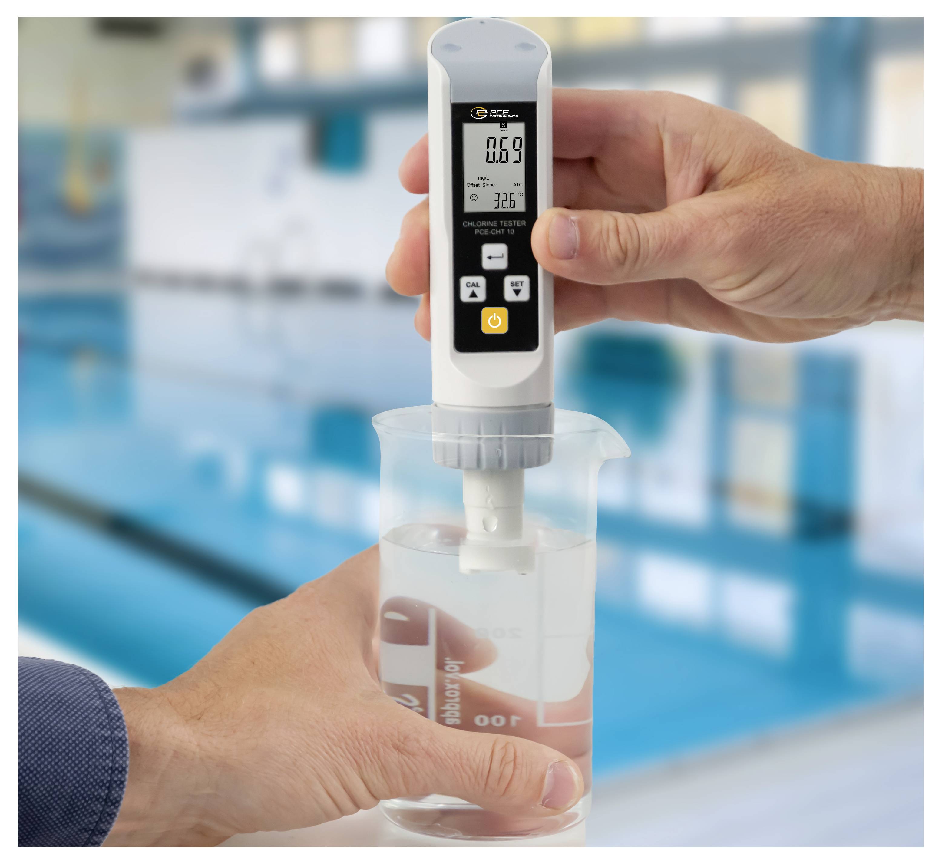 Eine Person misst die Wasserqualität mit einem digitalen Messgerät in einem Becherglas und liest die Werte 0,69 und 32,6 in einer Laborumgebung ab.
