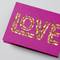 Rosa Karte mit dem Wort 'LOVE' in goldener, glitzernder Schrift.