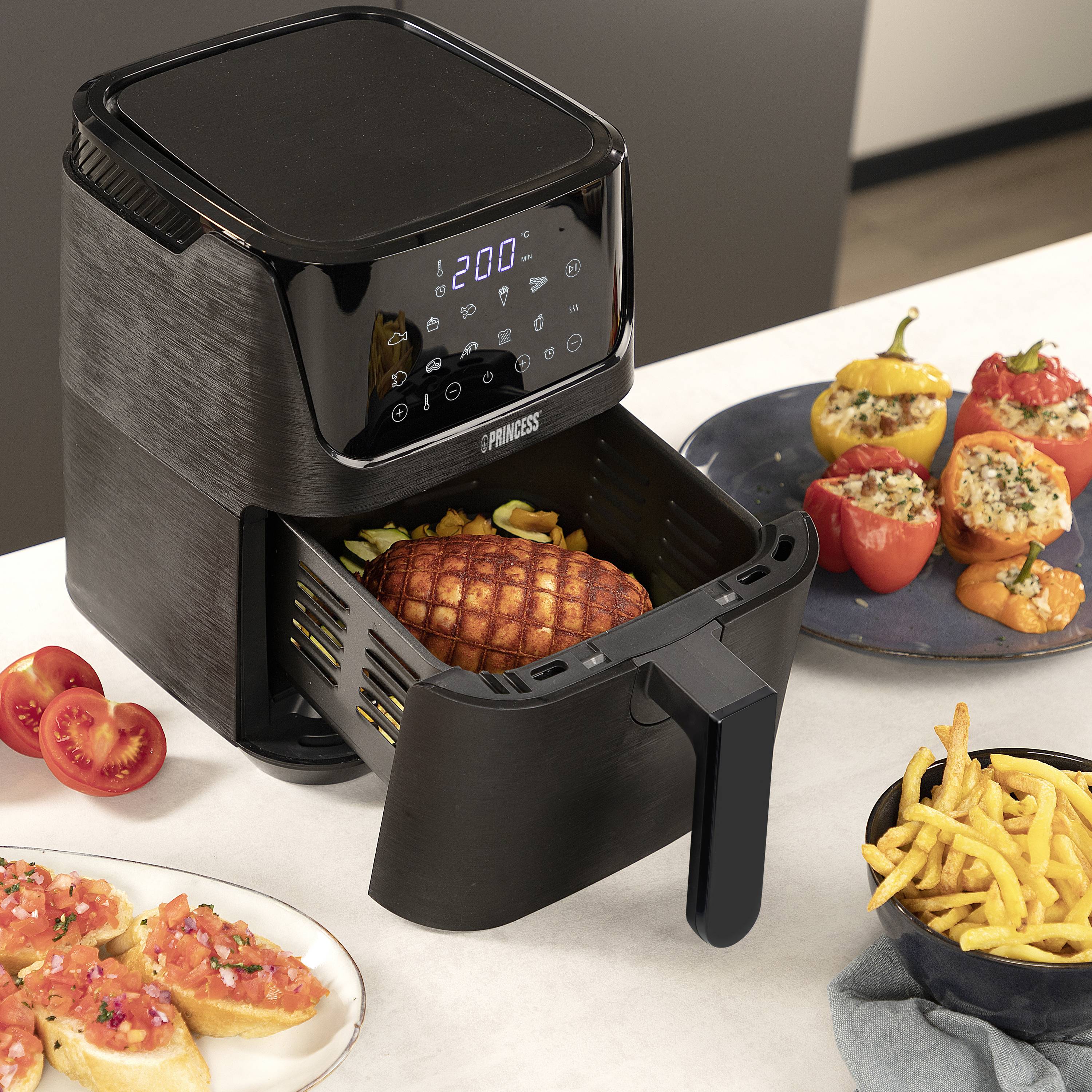 Eine Fritteuse mit geöffnetem Korb zeigt ein geformtes Gericht. Rechts gefüllte Paprika und Pommes auf einer Arbeitsplatte.