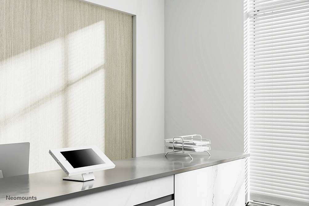 Modernes Büro mit hellen Wänden, Metalltisch, Tablet auf Ständer, Zeitungsständer, Fensterrollos; minimalistisches Design.