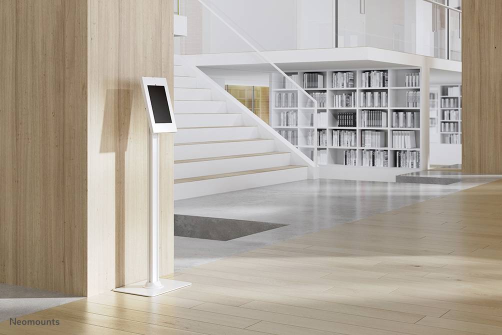 Ein Tablet auf einem Ständer steht in einem modernen, lichtdurchfluteten Raum mit Holzverkleidung, Treppe und Bücherregalen im Hintergrund.