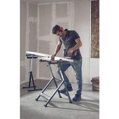 Ein Mann arbeitet mit Gehörschutz und Schutzbrille in einem teilausgebauten Raum. Er benutzt eine elektrische Säge, um ein Brett zu schneiden.