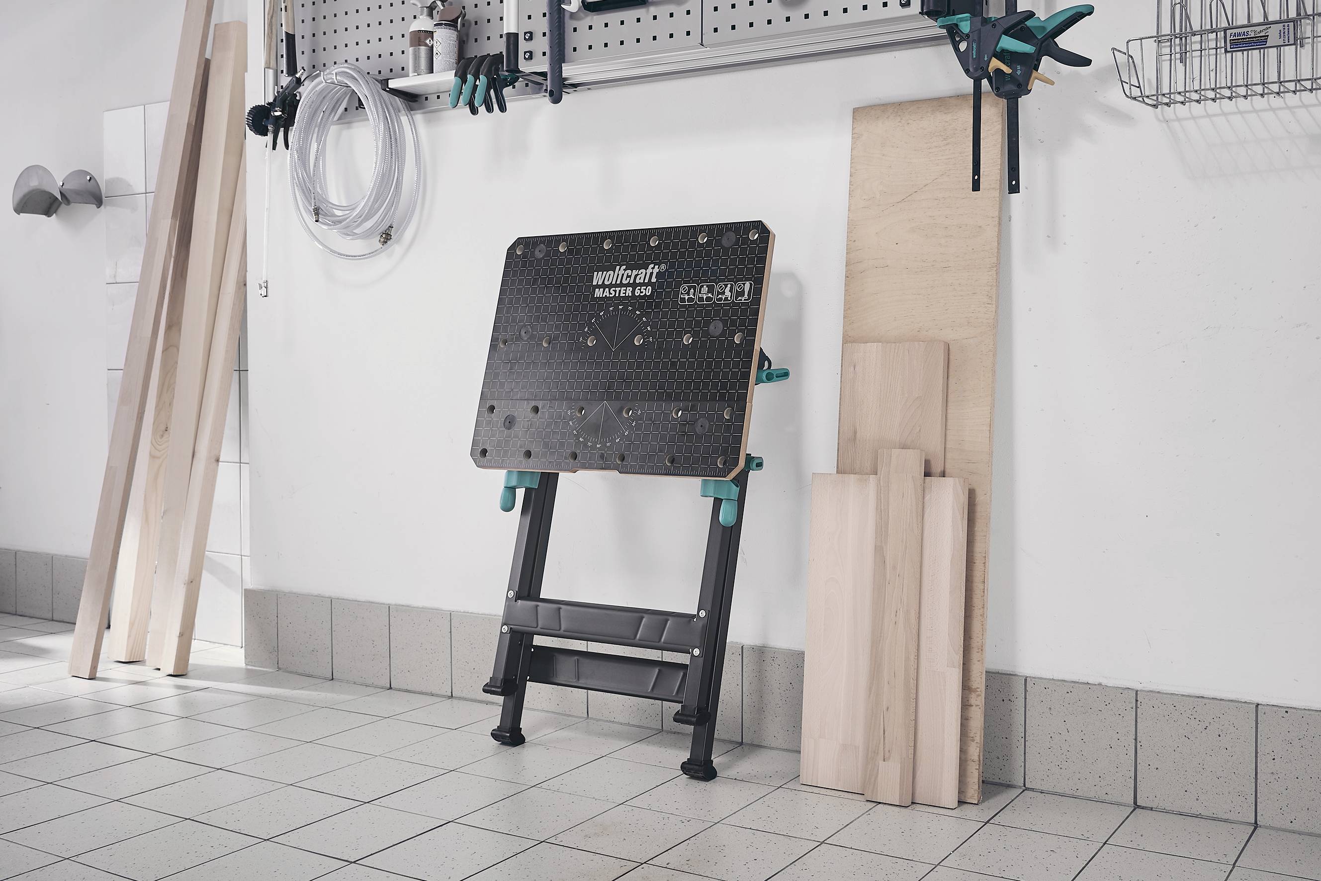 'Arbeitsplatz in einer Werkstatt mit Werkbank und Holzmaterialien an der Wand.'