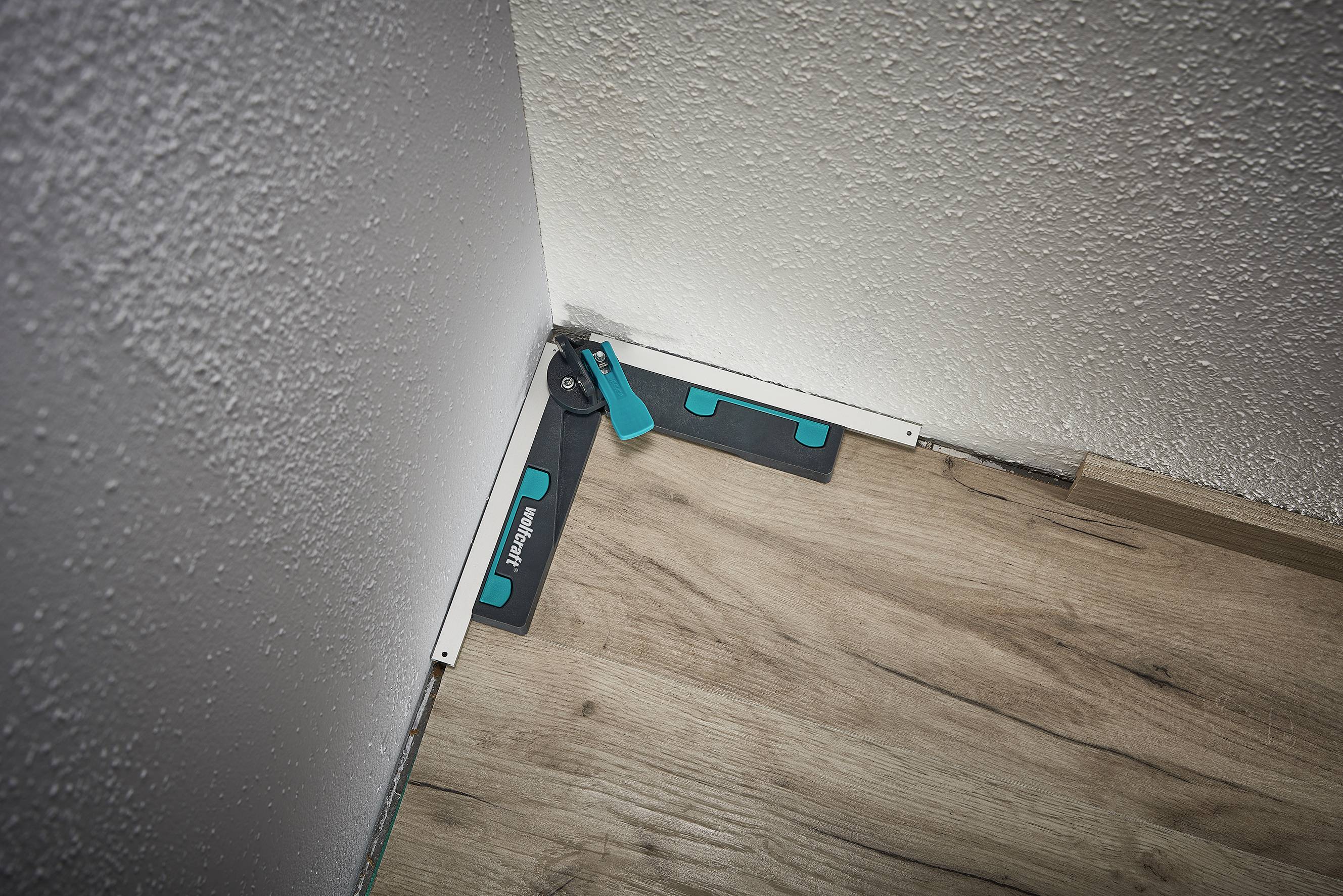 Werkzeug zur Verlegung von Laminat wird in einer Ecke eines Raumes verwendet. Ein grünes Abstandshalter-Set sorgt für gleichmäßigen Abstand zur Wand.
