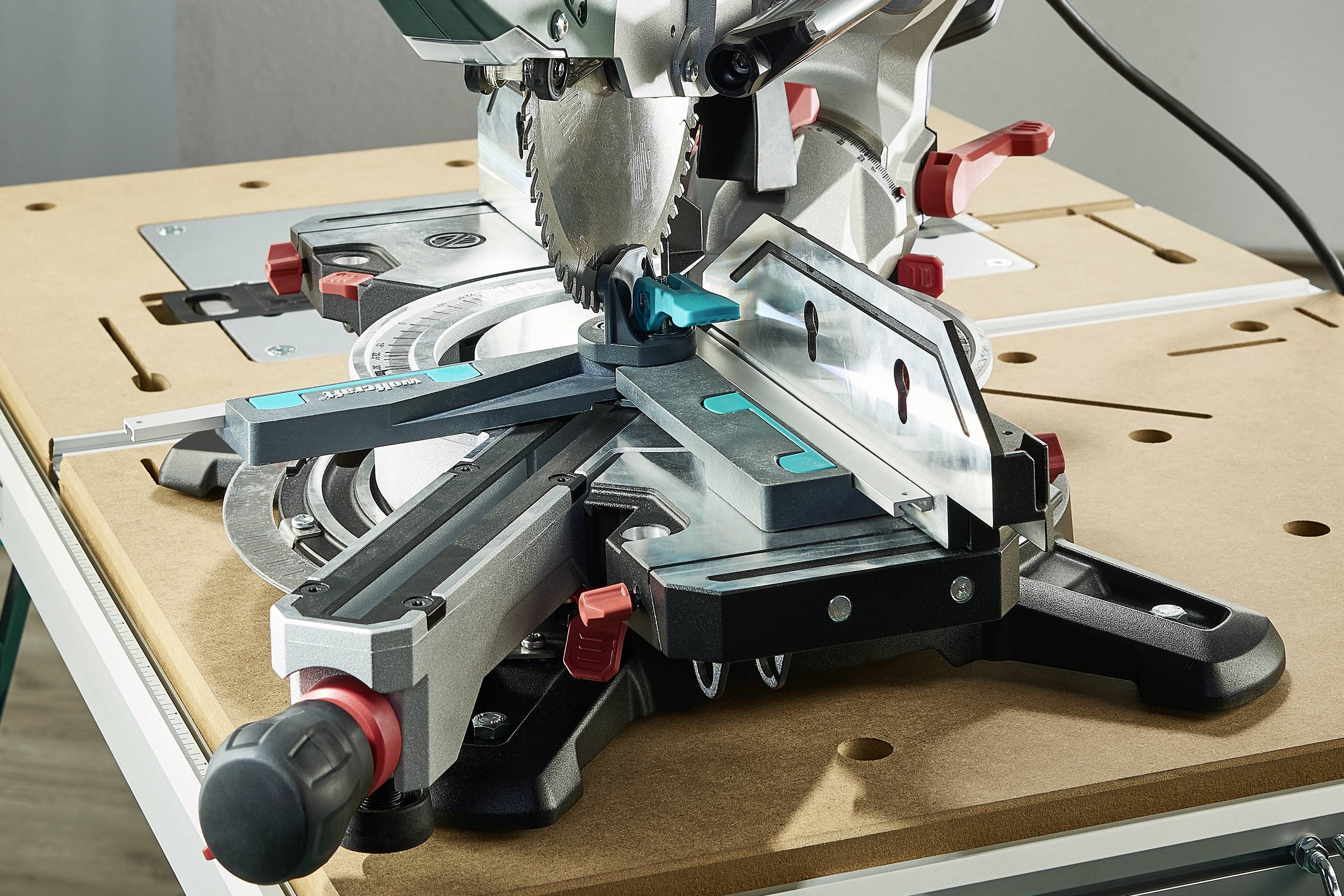 Eine Gehrungssäge auf einem Holztisch. Die Säge hat einen scharfen Metallblatt und mehrere Einstellknöpfe und Schienen für präzise Schnitte.
