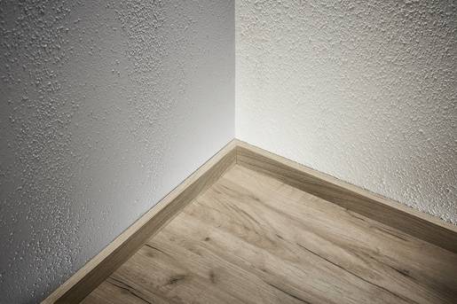 Ecke eines Raumes mit weißer Wand und Holzboden. Klarer Übergang zwischen Struktur der Wand und Textur des Bodens sichtbar.