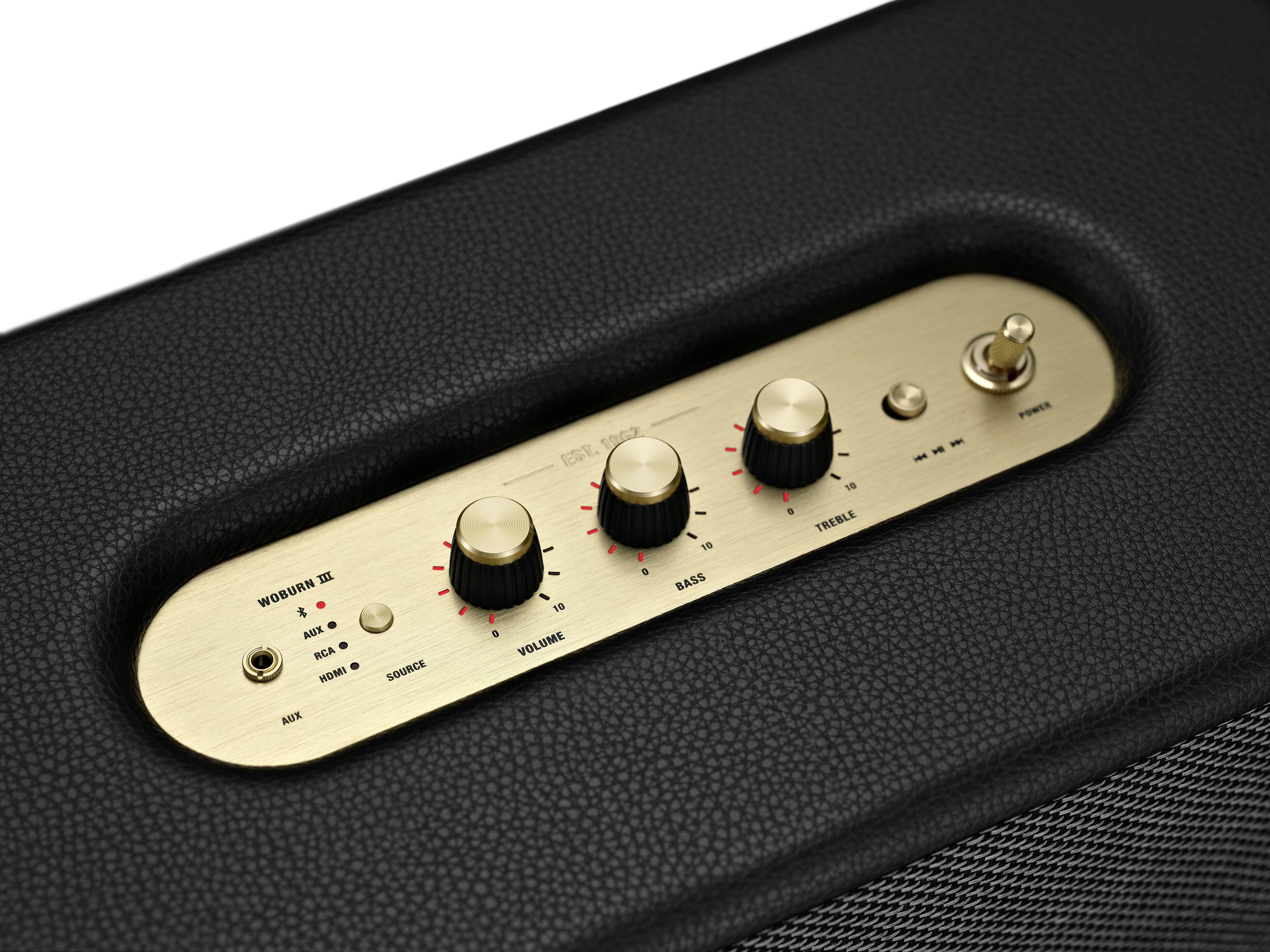 'Nahaufnahme eines schwarzen Lautsprechers mit goldener Bedienoberfläche, drei Reglern für Bass, Treble und Volume sowie einem Kippschalter.'