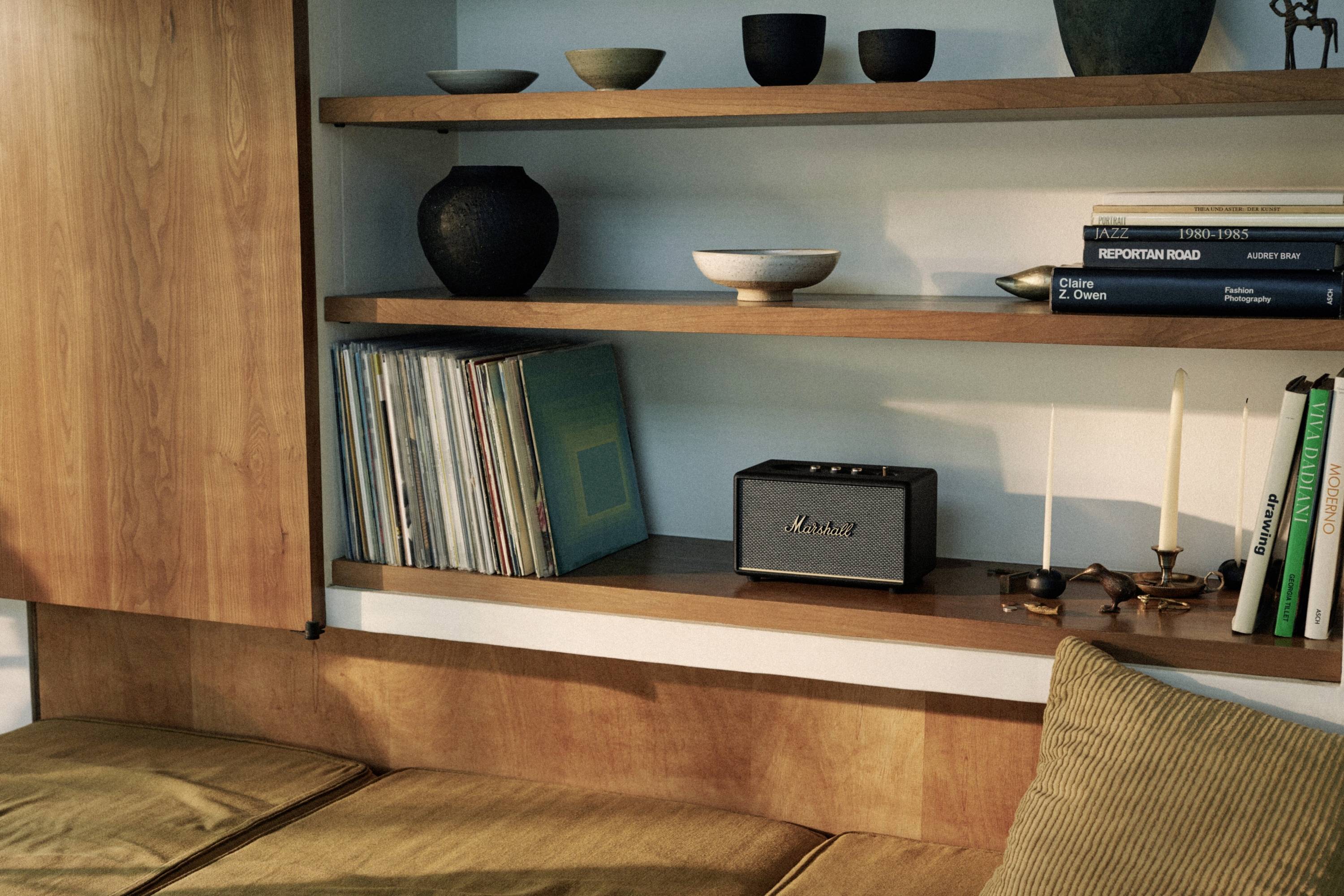 Ein Regal mit Büchern, Schallplatten, Kerzen und Keramik auf zwei Holzregalböden über einem Sofa.