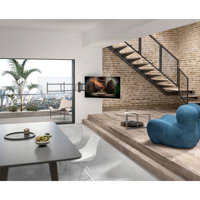 Moderner Wohnbereich mit Ziegelwänden und offener Treppe, gemütlichem blauen Sessel, Fernseher an der Wand und Blick auf eine Terrasse mit Stadtlandschaft.