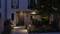 Moderne Hausfassade bei Nacht mit beleuchtetem Eingang und gepflegtem Garten; Hausnummer 21 sichtbar.