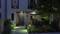 Eingangsbereich eines modernen Hauses bei Nacht, beleuchtet von Weglichtern, umgeben von gepflegtem Garten mit blühenden Pflanzen.