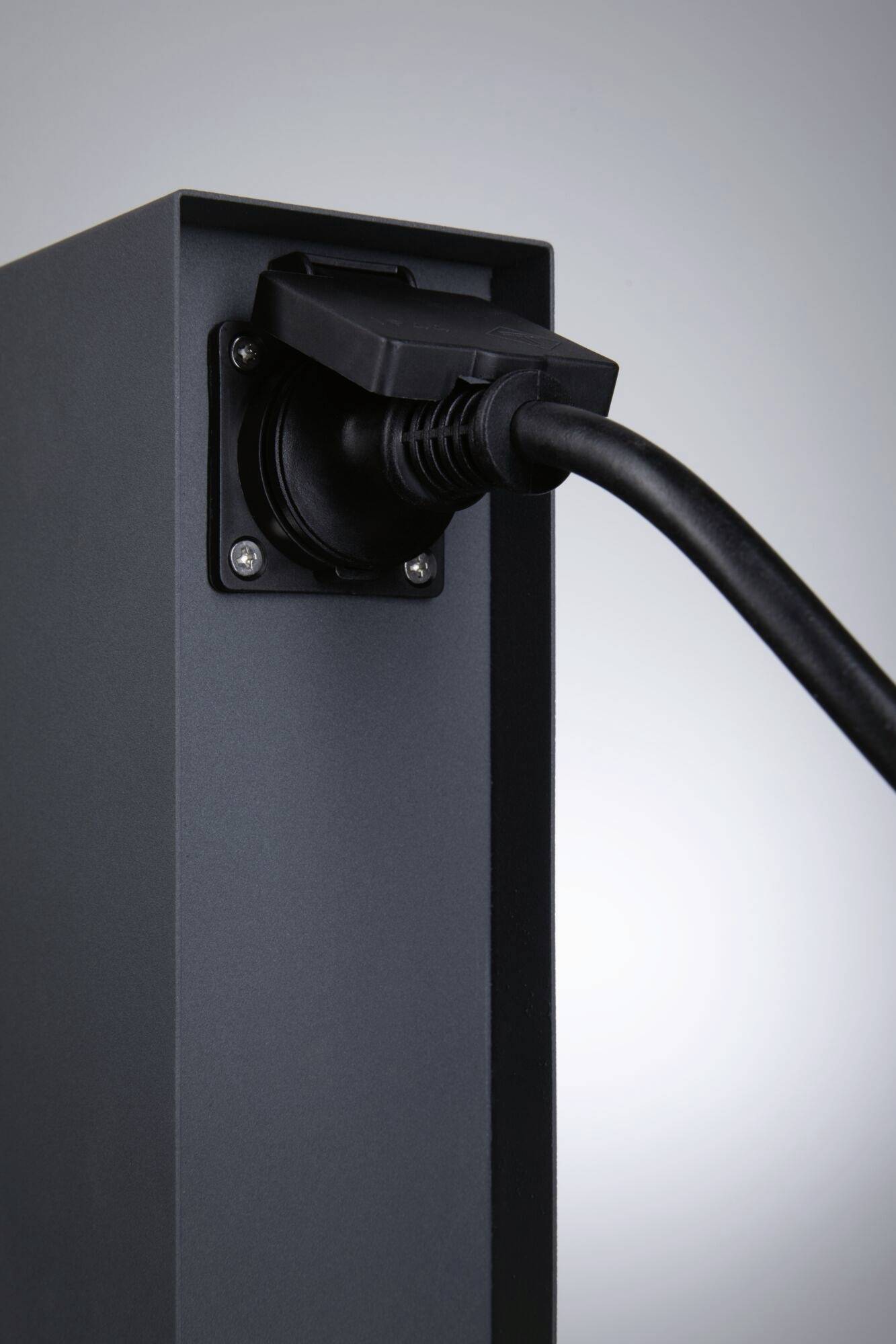 Ein schwarzes Stromkabel ist in eine schwarze Steckdose an einem grauen Ständer eingesteckt.