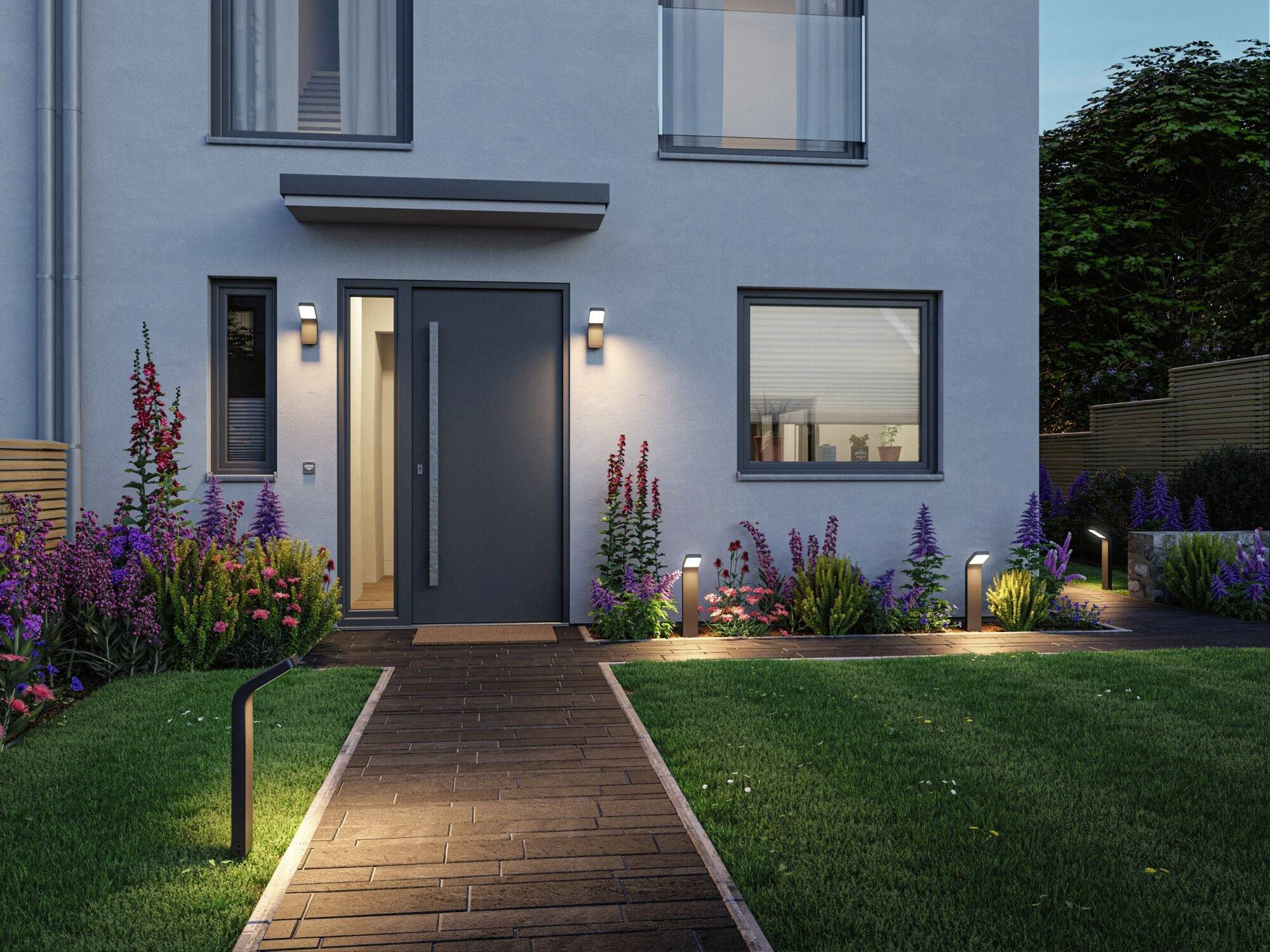 Eingangsbereich eines modernen Hauses bei Abenddämmerung, umgeben von blühenden Pflanzen und dezent beleuchtetem Gehweg.