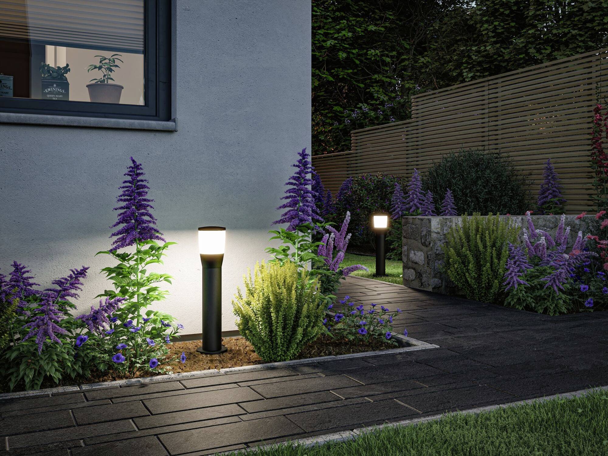 Gartenweg mit blühenden Pflanzen und modernen Gartenlampen, die bei Dämmerung leuchten. Ein Haus ist im Hintergrund sichtbar.
