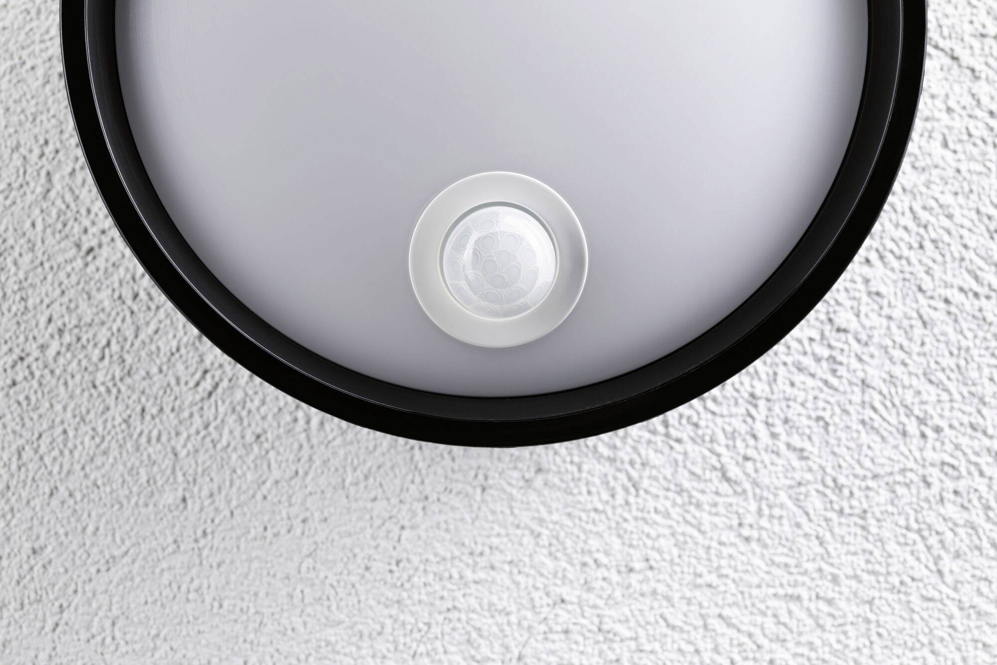 Runde Deckenleuchte mit Bewegungsmelder darauf montiert. Der Bewegungsmelder befindet sich zentral an der Unterseite der Lampe.