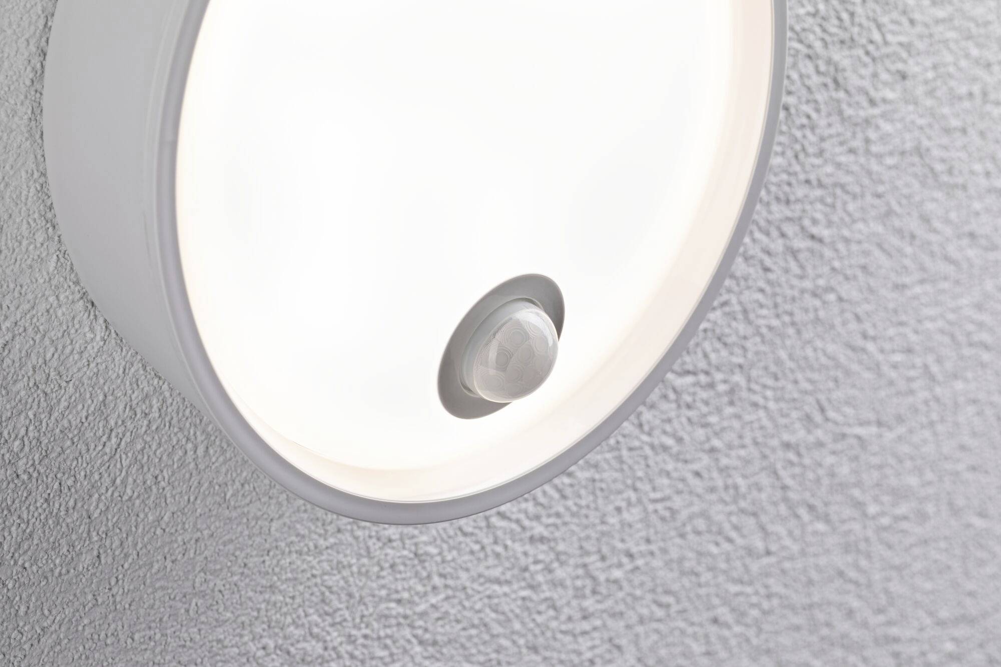Runde Deckenlampe mit Bewegungssensor an weißer, strukturierten Decke befestigt, leuchtet hell.