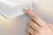'Eine Hand drückt eine kreisförmige Taste an einer weißen Wandleuchte.'
