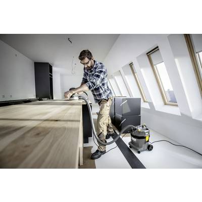 Ein Mann schleift eine Holzplatte in einer modernen, hellen Küche. Ein Staubsauger steht neben ihm, um den Staub aufzufangen.