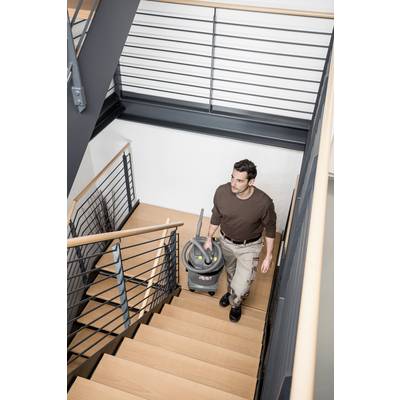 Eine Person trägt einen Staubsauger eine Holztreppe in einem modernen Gebäude mit Metallgeländer hinauf.