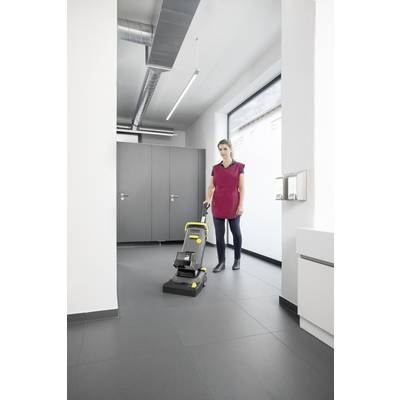 Eine Person reinigt den Boden in einem modernen Raum mit einer elektrischen Reinigungsmaschine. Im Hintergrund sind Fenster und Türen zu sehen.