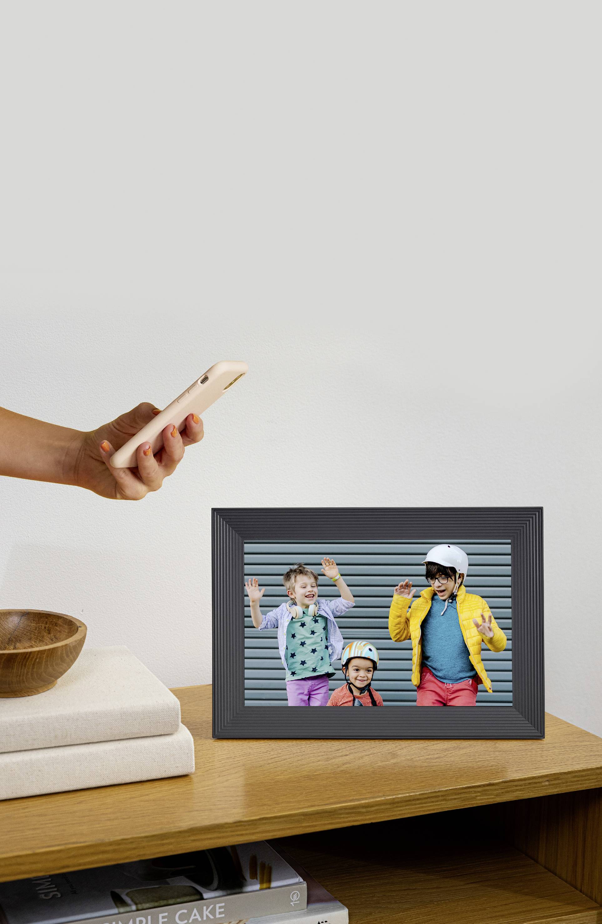 Eine Person mit Smartphone fotografiert ein gerahmtes Bild auf einem Tisch. Im Bild: Drei lachende Kinder, eins mit Helm.