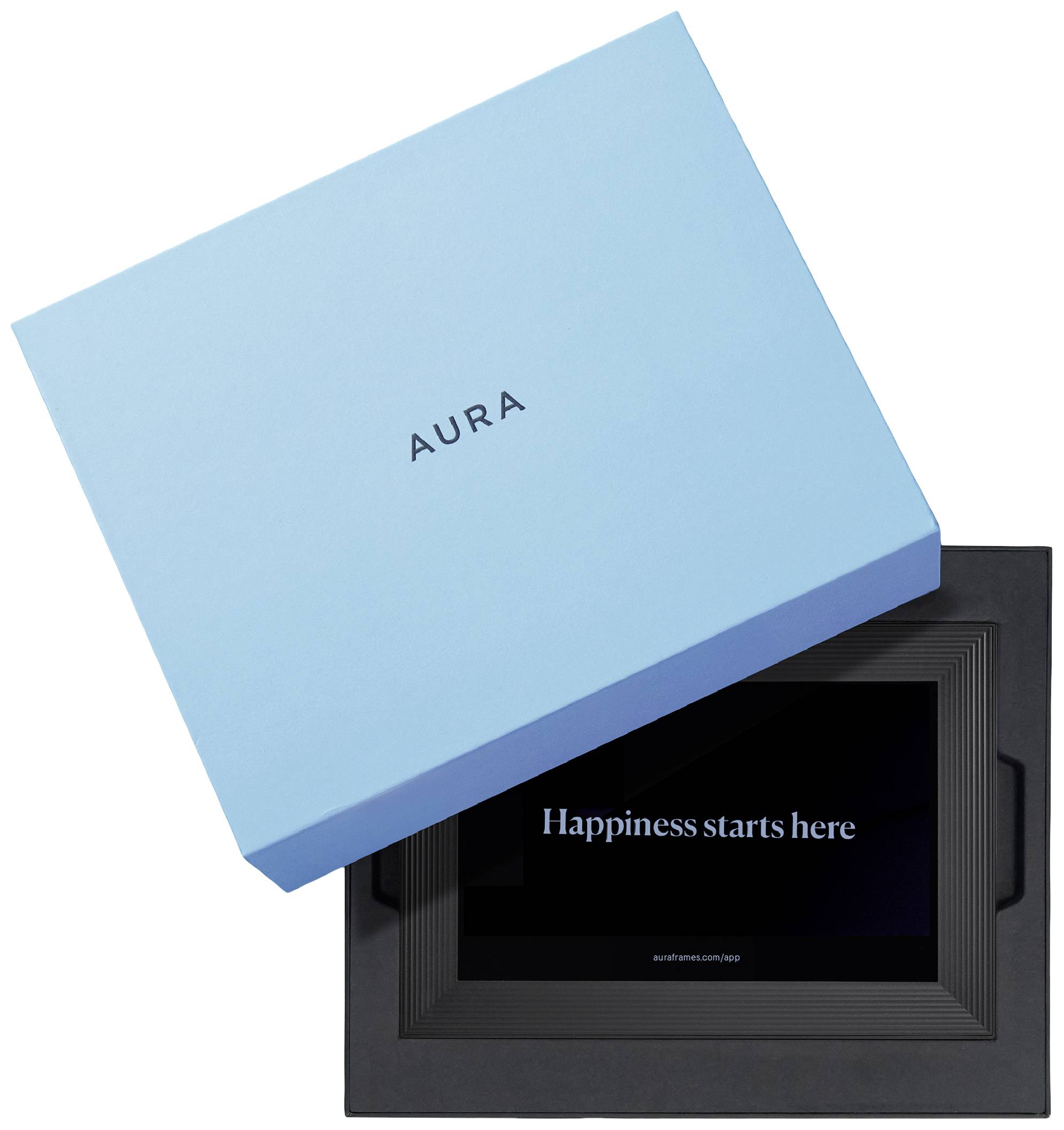 Eine schwarze elektronische Bilderrahmen mit der Aufschrift 'Happiness starts here'. Daneben liegt eine geschlossene blaue Box mit dem Schriftzug 'Aura'.