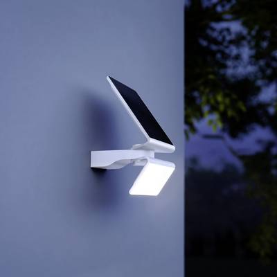 Eine moderne Wandlampe mit Solarmodul leuchtet im Dunkeln. Die Lampe ist an einer grauen Außenwand montiert.