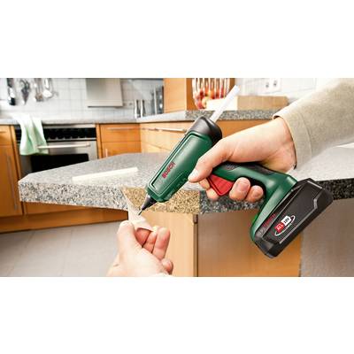 Eine Person verwendet eine Akku-Heißklebepistole, um ein Stück Holz an der Kante einer Küchenarbeitsplatte zu befestigen.