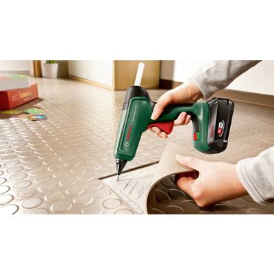 Eine Person benutzt eine kabellose Heißklebepistole, um ein Stück Linoleum auf einem strukturierten Boden zu verkleben.