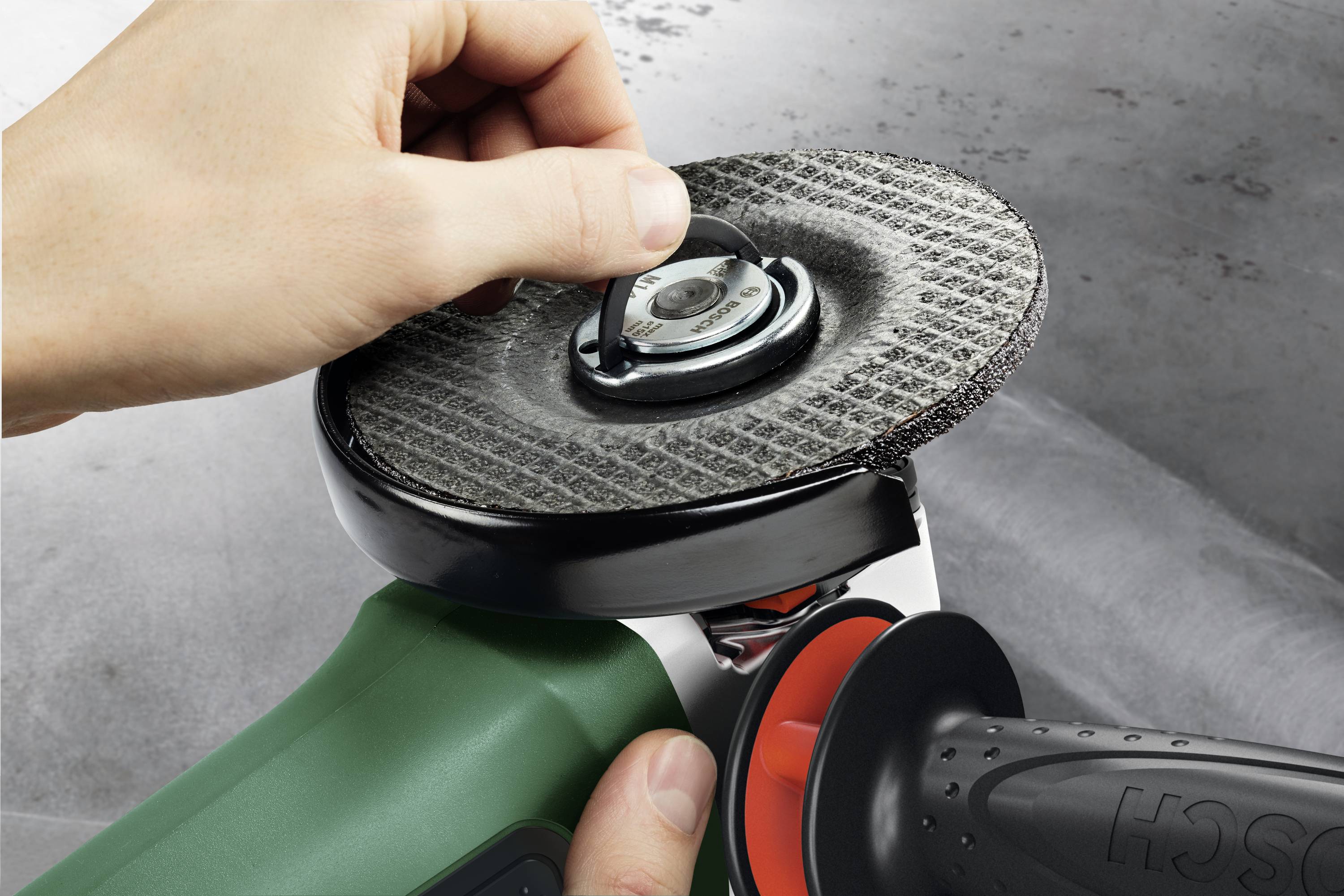 Eine Hand befestigt eine Schleifscheibe an einem Winkelschleifer. Der Hintergrund ist unscharf, der Fokus liegt auf dem Werkzeug.