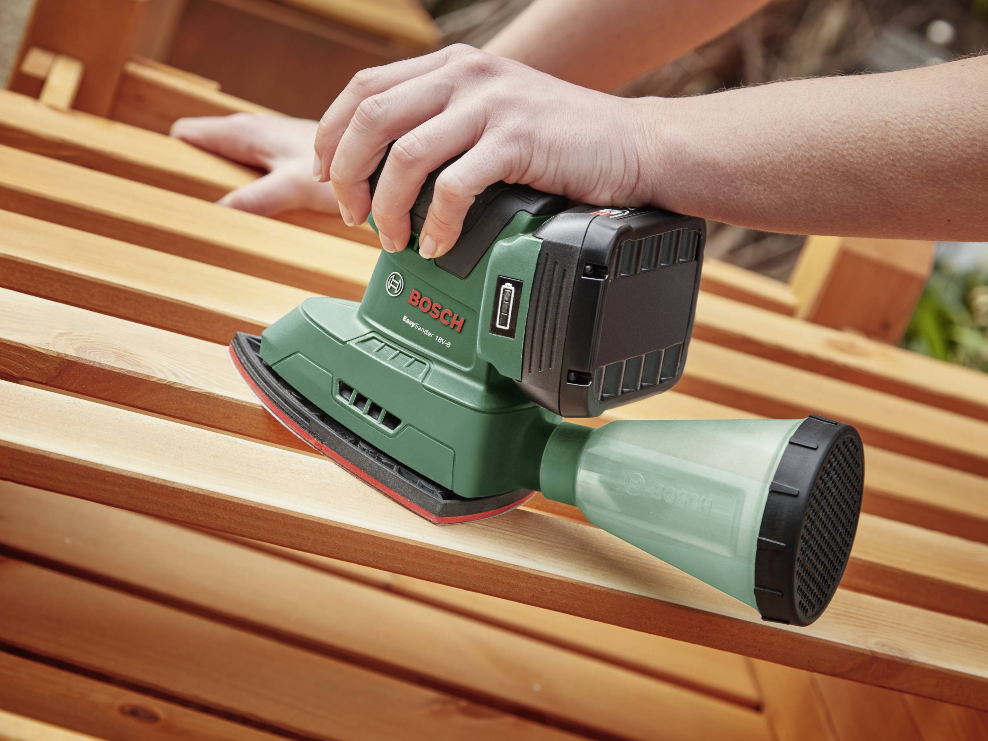 Person schleift Holzoberfläche mit einem grünen, kabellosen Bosch Schleifgerät, das in der Hand gehalten wird.