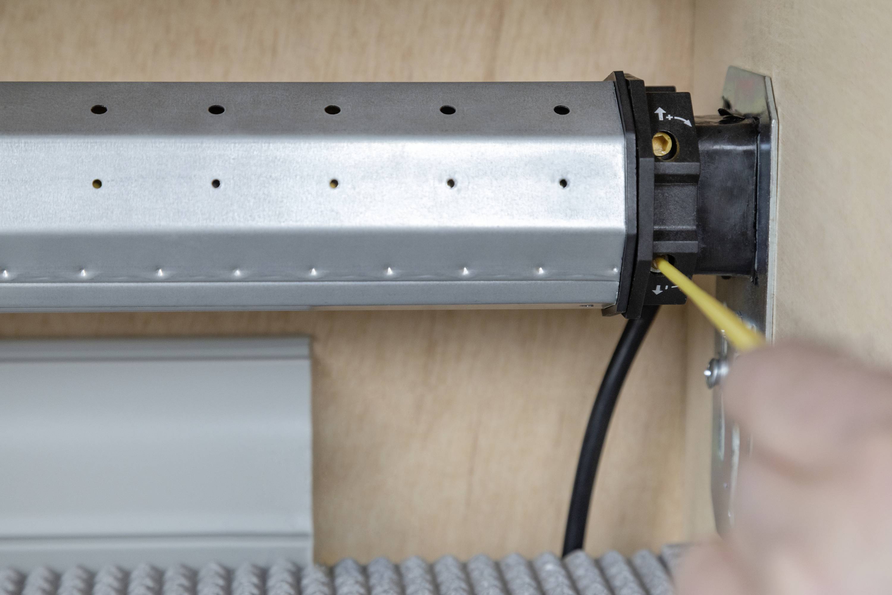 Ein Mensch justiert ein Metallteil mit einem gelben Werkzeug. Das Teil ist fest montiert und mit Kabeln versehen.