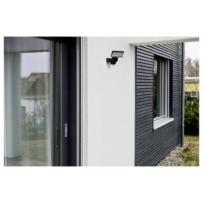 Außenansicht eines modernen Hauses mit einer Glasschiebetür, einer wandmontierten Leuchte und dunkler Verkleidung neben einem Fenster mit Kieslandschaftsbau.