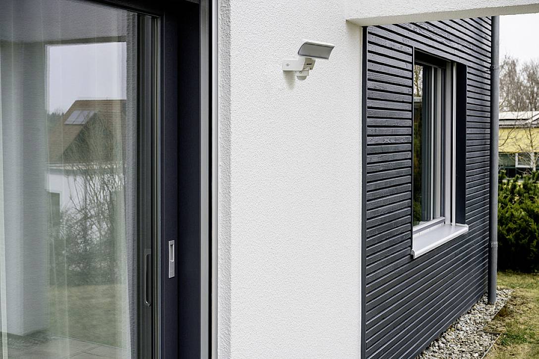Hellgraues, modernes Haus mit dunklen Akzenten, Schiebefenstern und einer Außenleuchte.