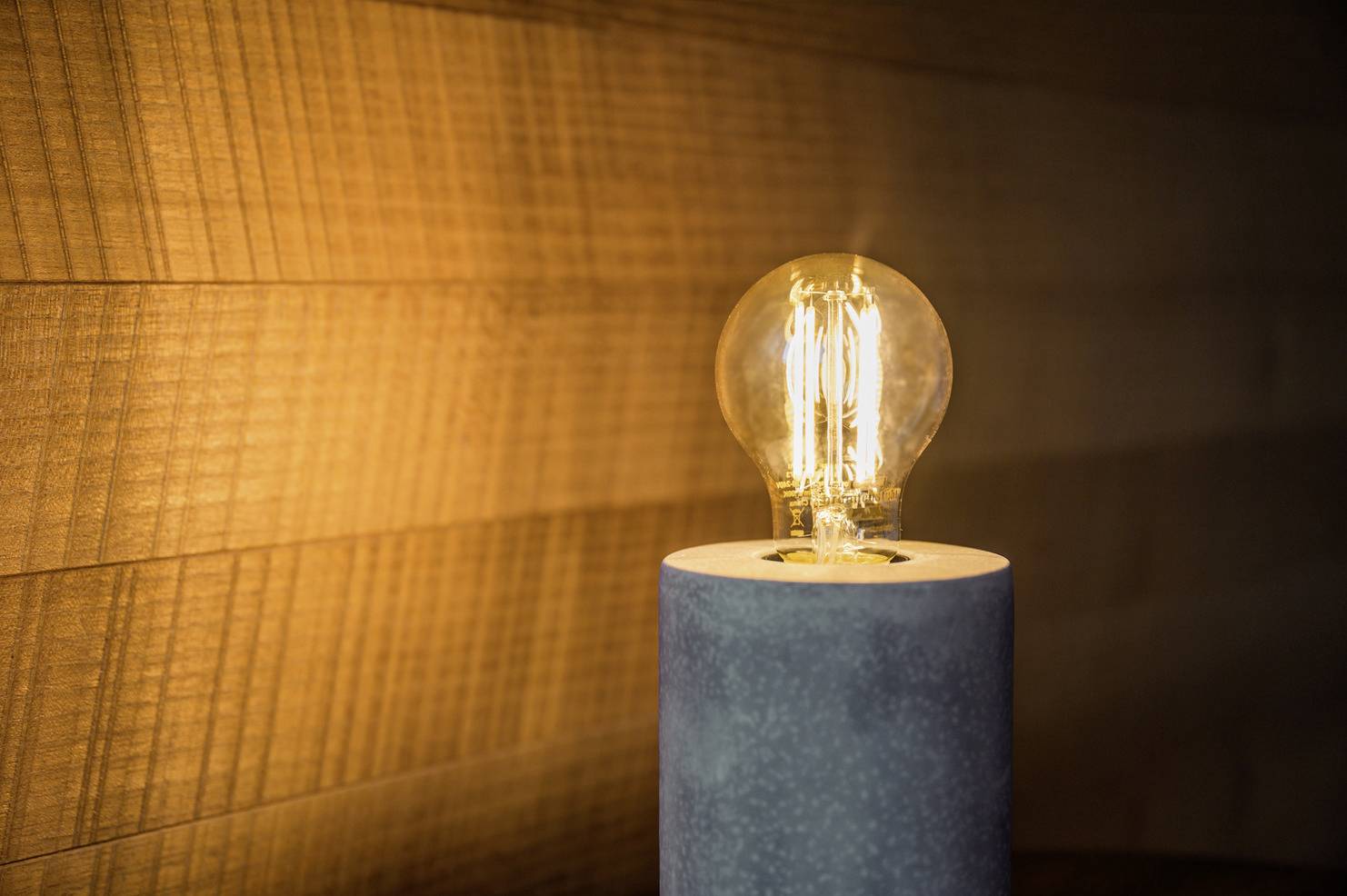 Eine Glühbirne in einem modernen, minimalistischen Lampensockel leuchtet warm gegen eine Holzwand und schafft eine gemütliche Atmosphäre.