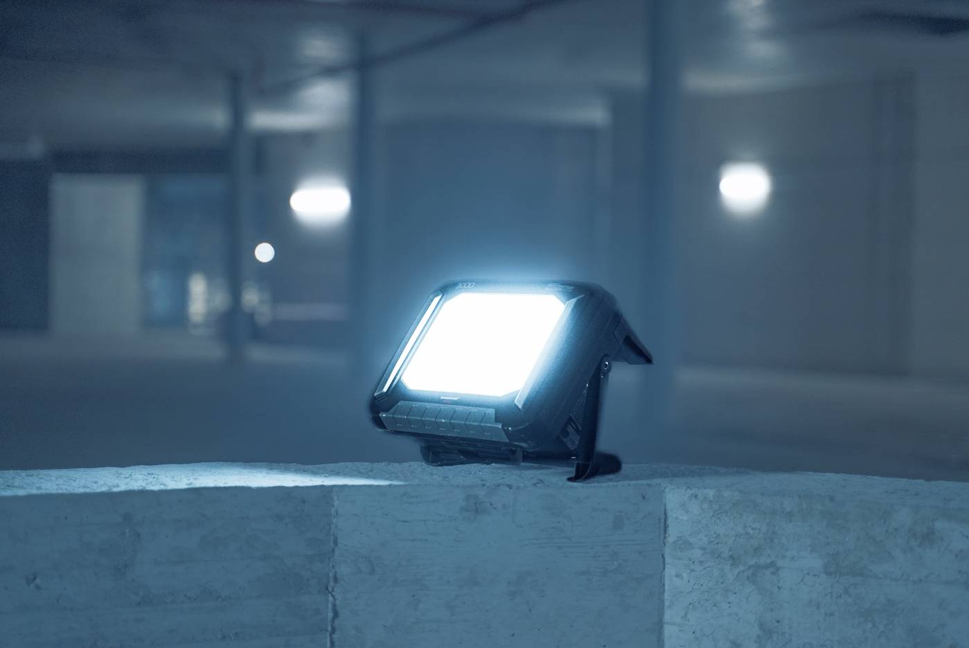 Ein leuchtender LED-Strahler auf einer Betonoberfläche in einer dunklen, leeren Garage, erzeugt bläuliches Licht in der Umgebung.