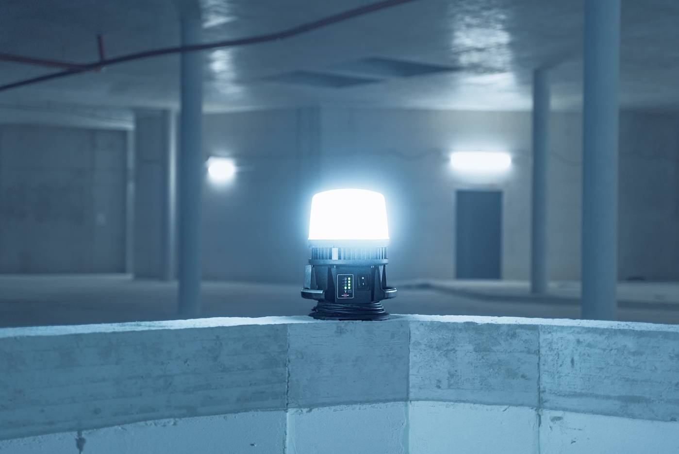Eine leuchtende Lampe steht auf Beton in einem leeren, halbdunklen Raum mit sichtbaren Stützsäulen und Decke.