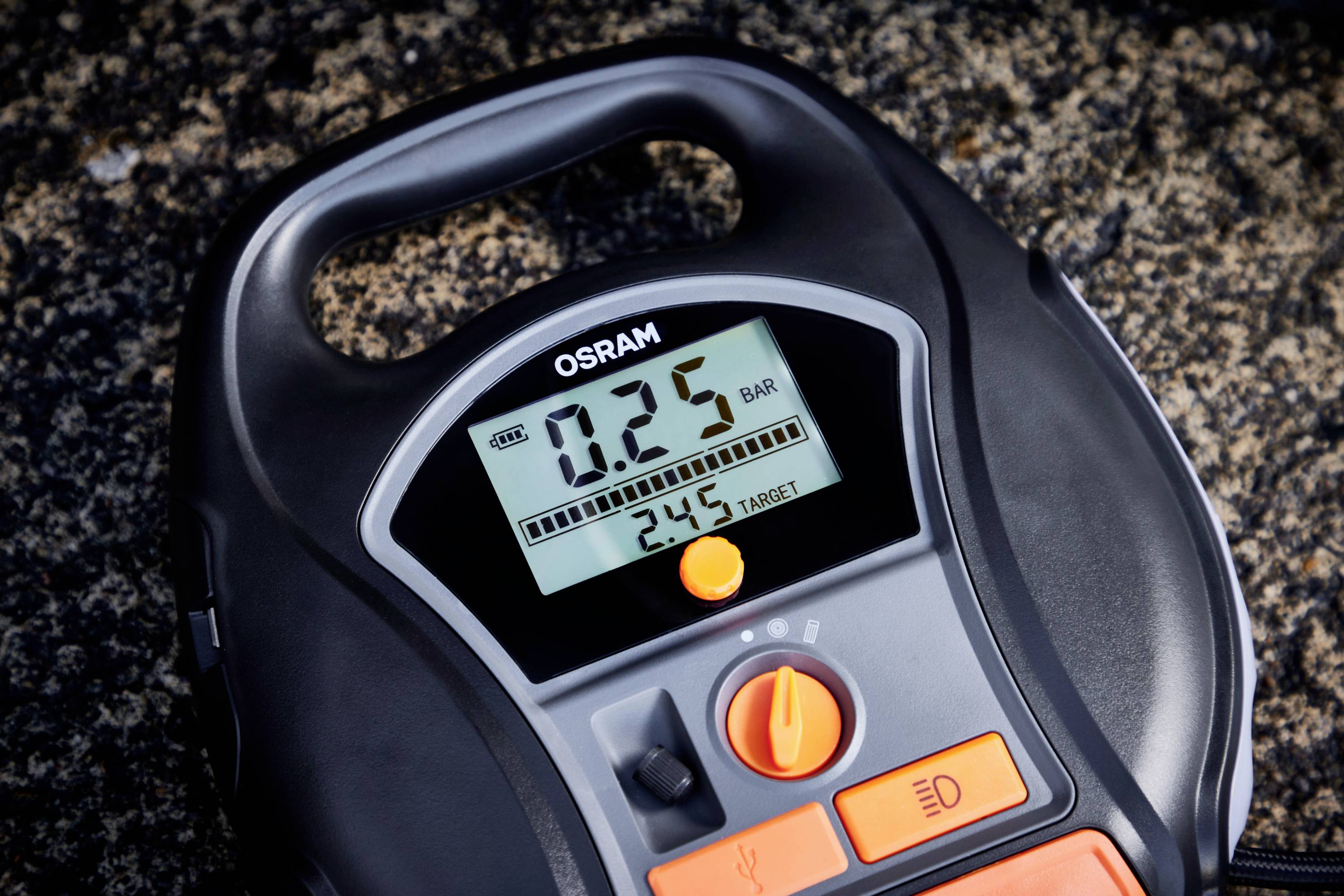 Tragbarer, digitaler Reifenfülldruckmesser von OSRAM zeigt 0,25 Bar an; Zielwert 2,45 Bar. Gerät liegt auf Granitoberfläche.