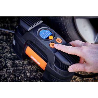 Person drückt den Power-Knopf eines digitalen Reifenfüllers, der neben einem Autoreifen liegt. Anzeige zeigt '0.0'.