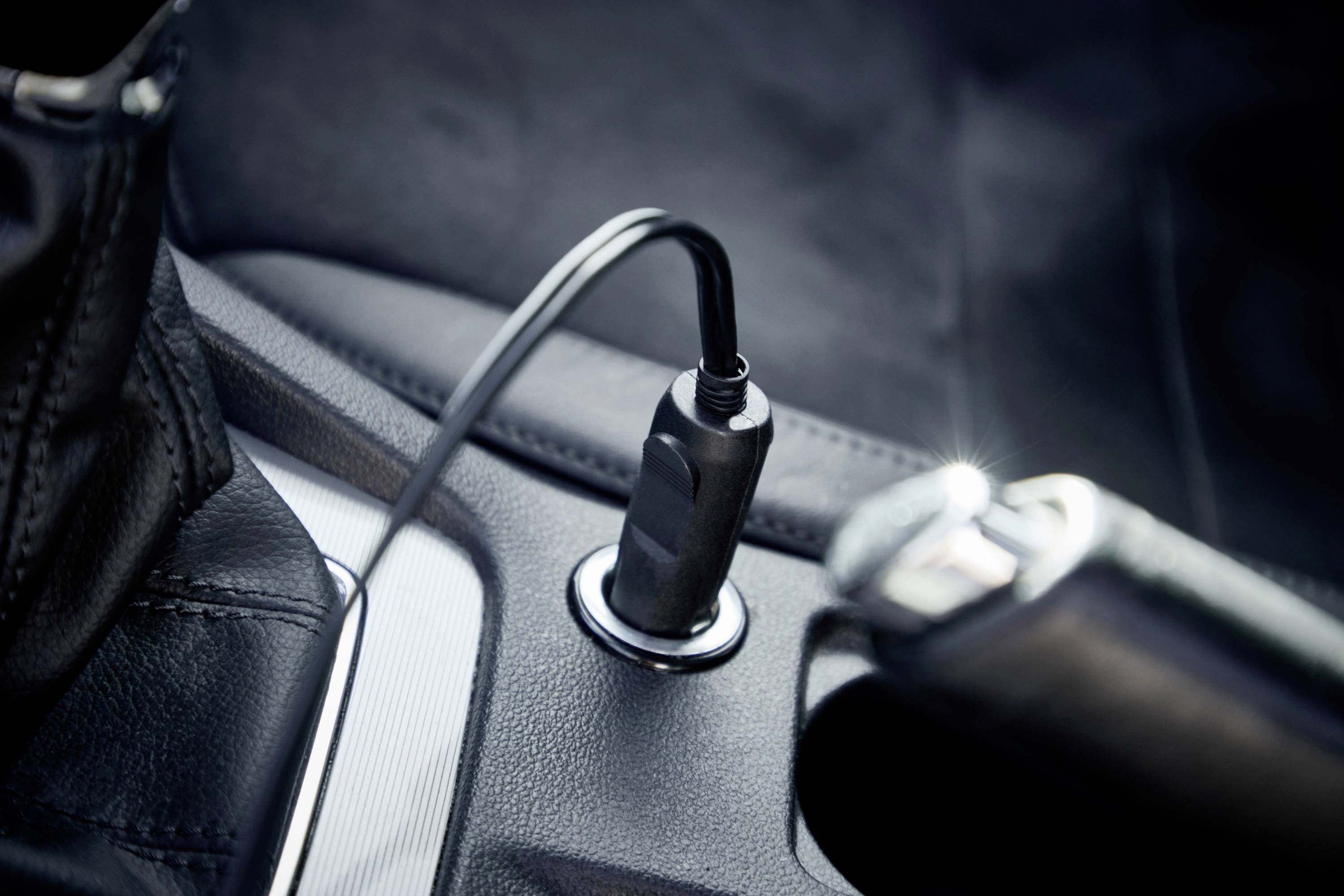 Ein Ladekabel steckt in einer Autosteckdose. Das Foto zeigt eine Nahaufnahme im Fahrzeuginnenraum mit Fokus auf die Steckverbindung.