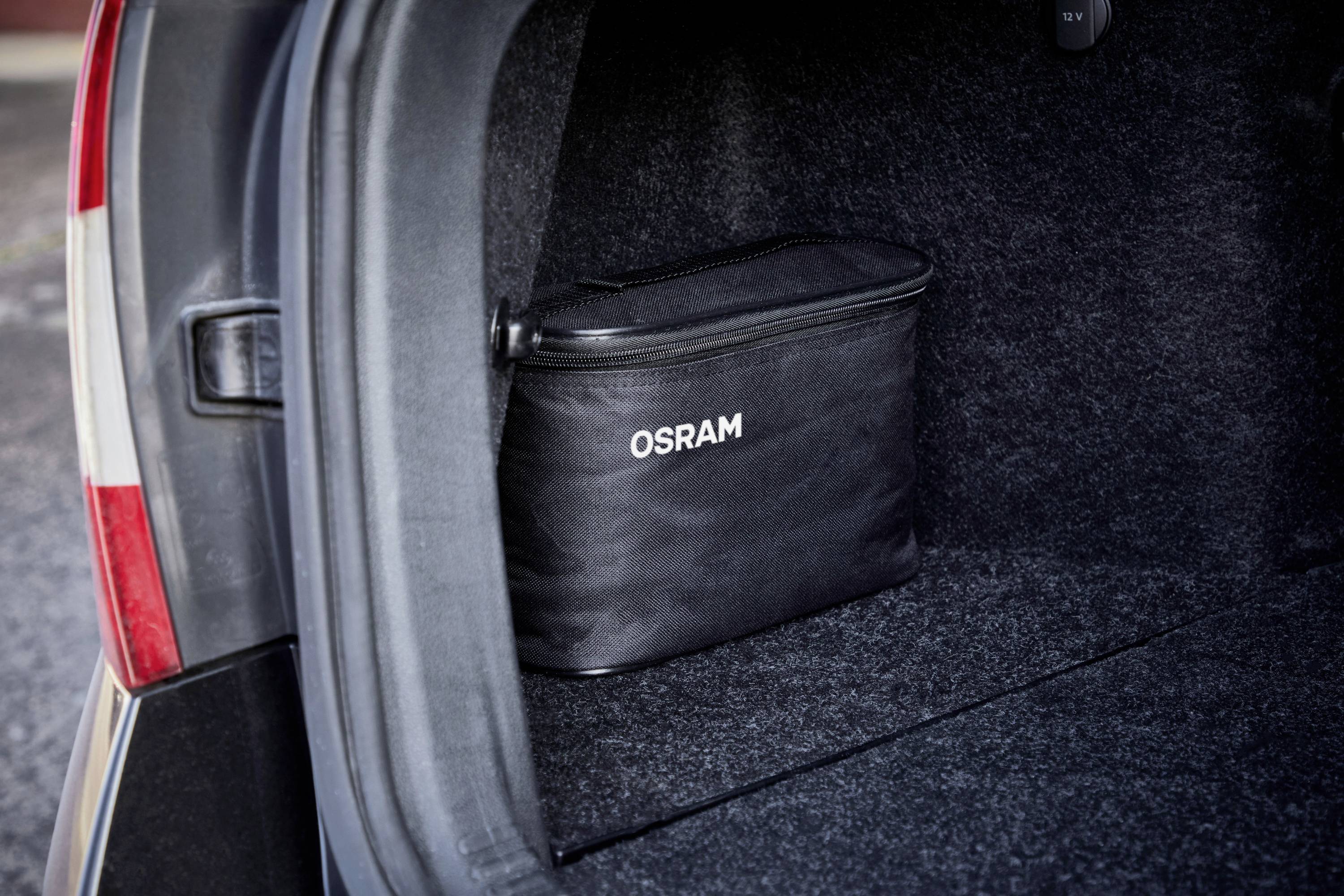 Kofferraum eines Autos mit einer schwarzen Tasche, auf der 'OSRAM' steht. Die Tasche steht auf dem Teppichboden des Kofferraums.