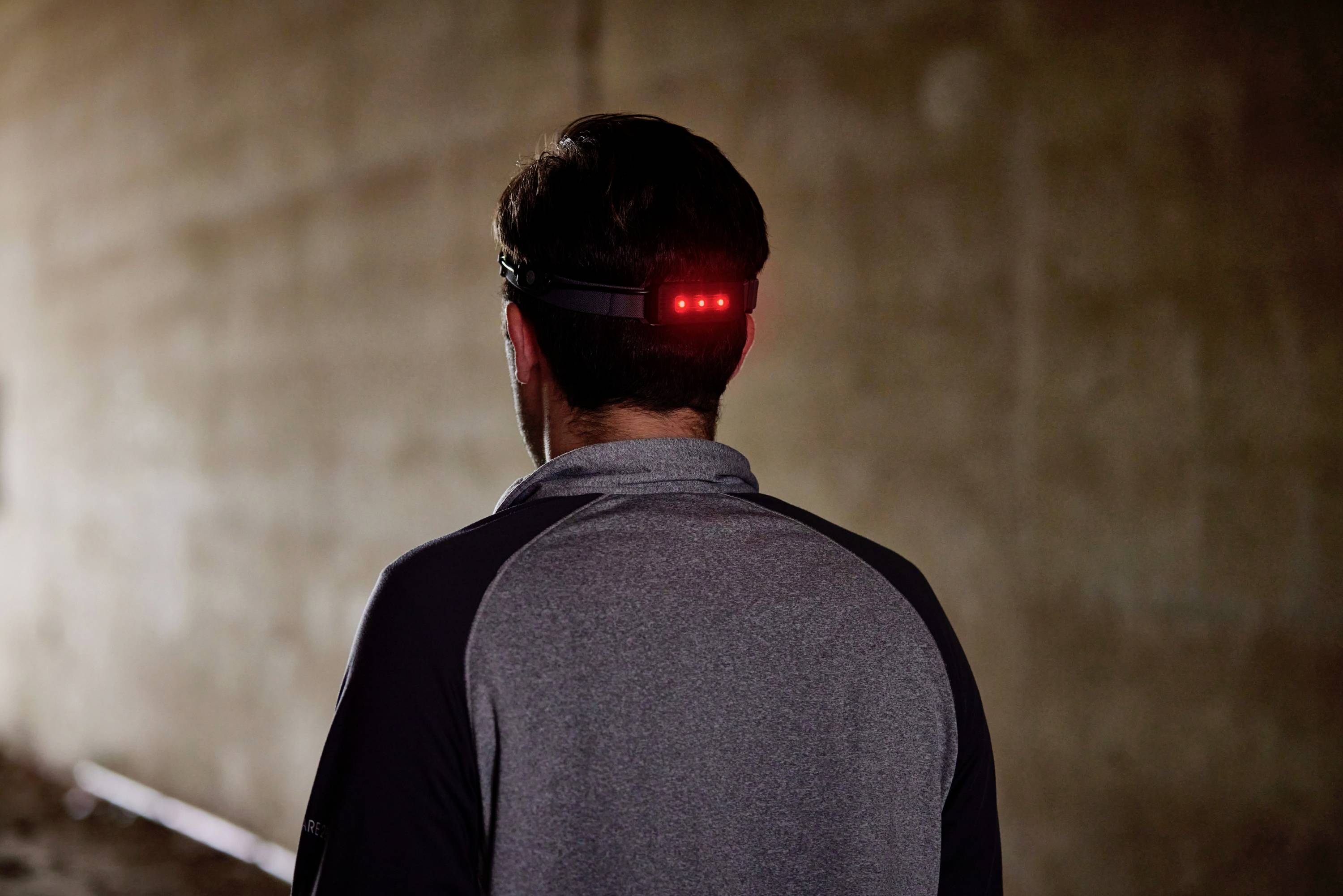 Eine Person in einem grauen Oberteil geht in einem dunklen Tunnel. Ein rotes Licht leuchtet hinten an ihrem Stirnband.
